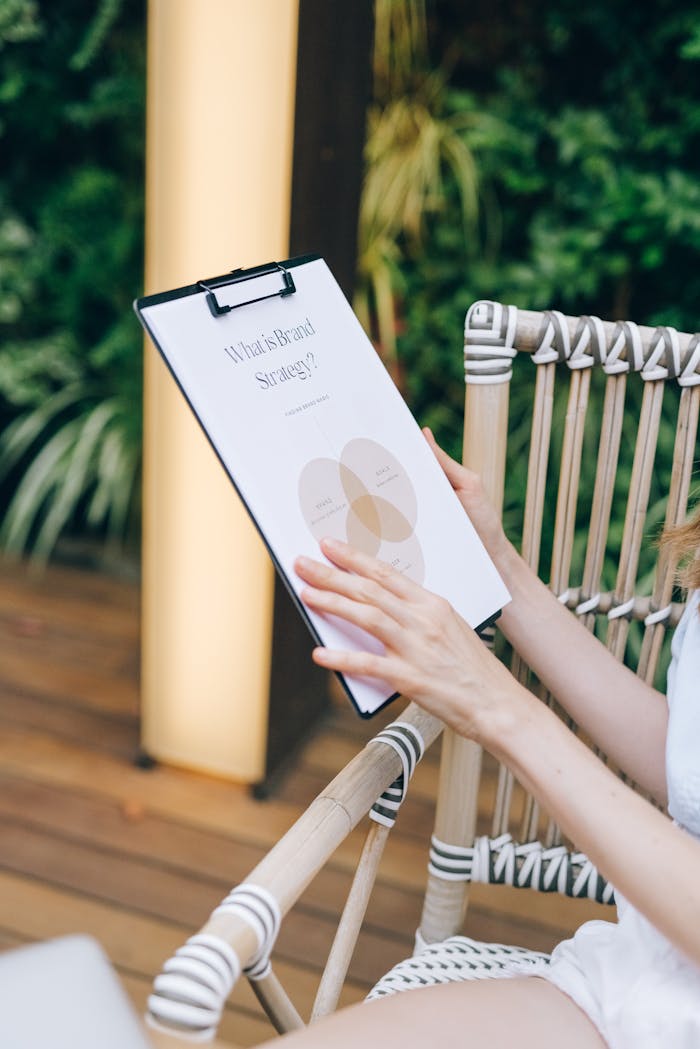 An individual holds a clipboard with a brand strategy document, sitting outdoors in an informal setting.